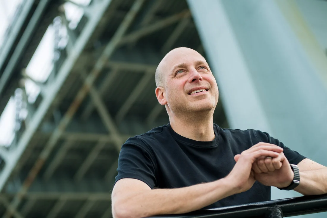 NYC Branded lifestyle portrait Speaker Lou Diamond standing under Triboro Bridge smiling