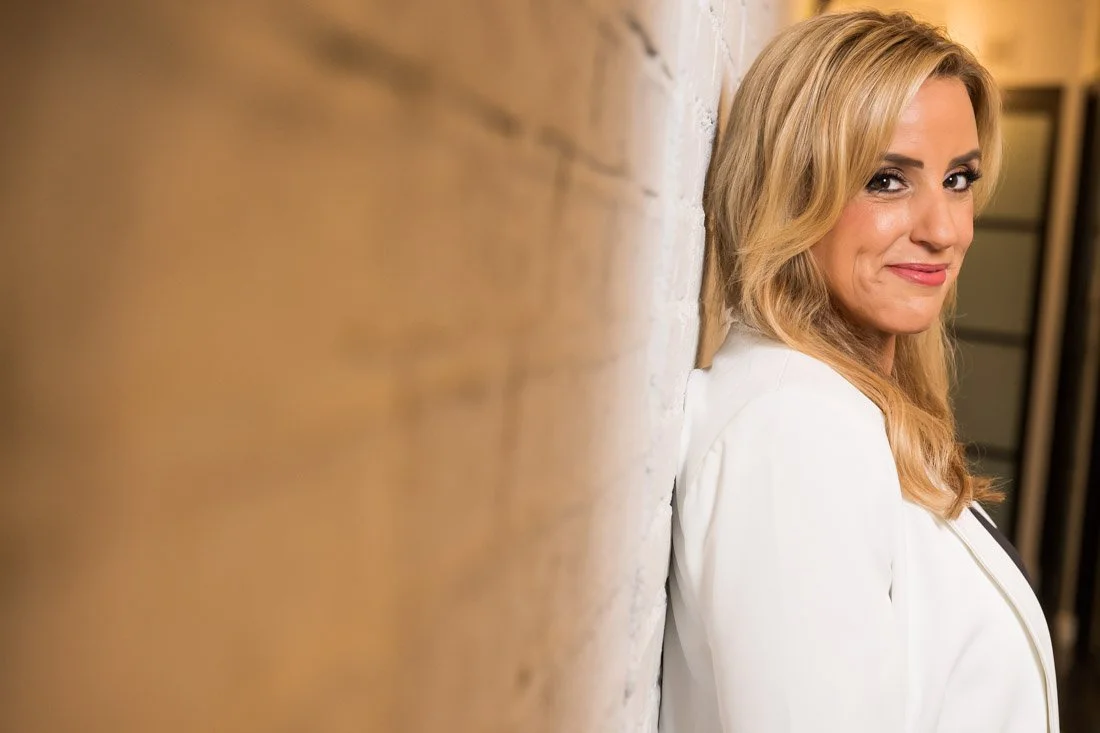personal brand photo speaker expert Rachel DeAlto leaning against bricks smirk smiling to camera