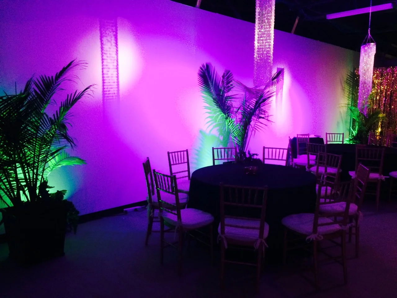 Acrylic crystal chandeliers act as room decor and floating centerpieces. LED uplighting in fuchsia and green added bold color to plain white walls. 