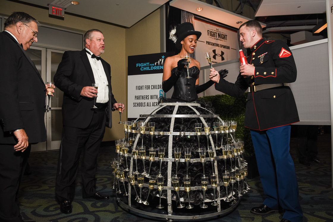 Ensconced in a champagne flute cage, Tina Brown doles out drinks to Lance Corporal Reid Norfolk and other guests during the Fight Night benefit cocktail hour.