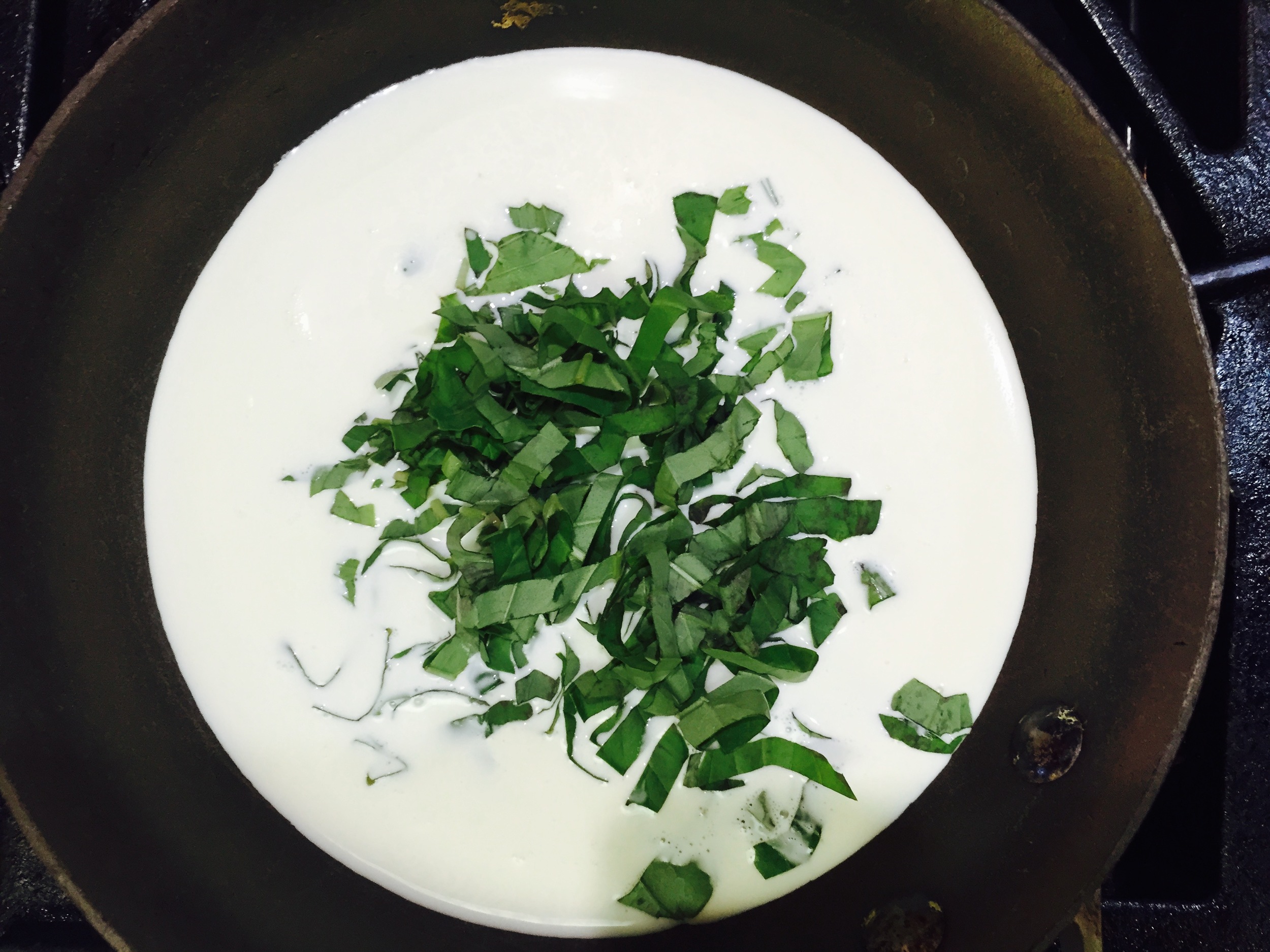 Chiffonade of basil in cream ready to be heated.