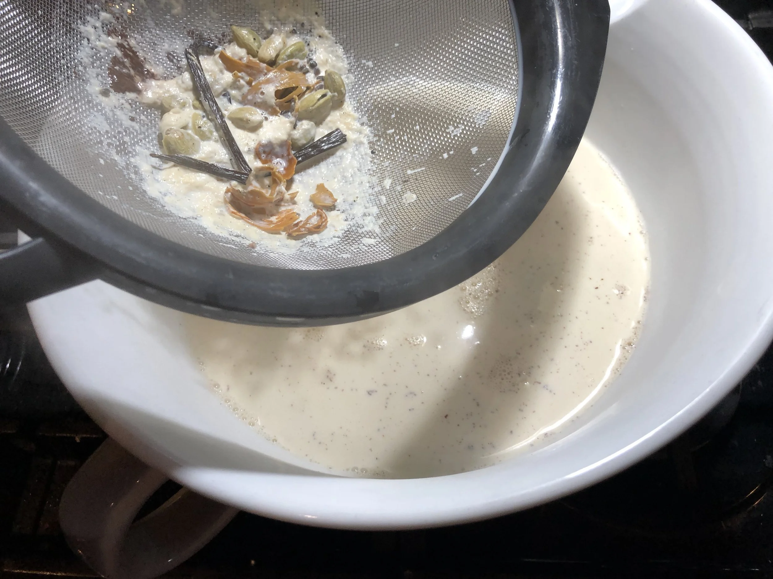 Straining out the crushed cardamom, blade mace, and split vanilla bean.