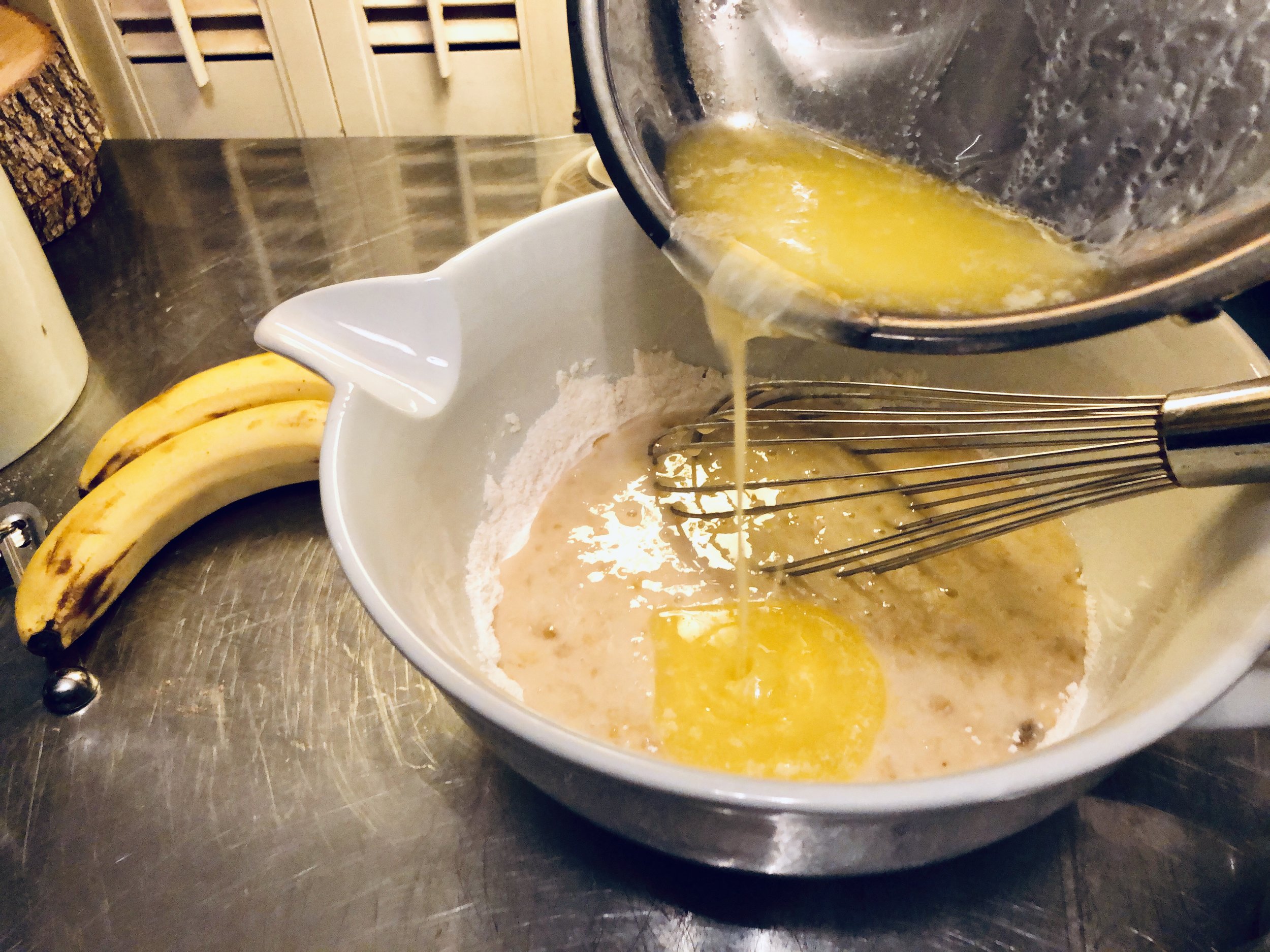Adding the melted butter to the banana cake batter.