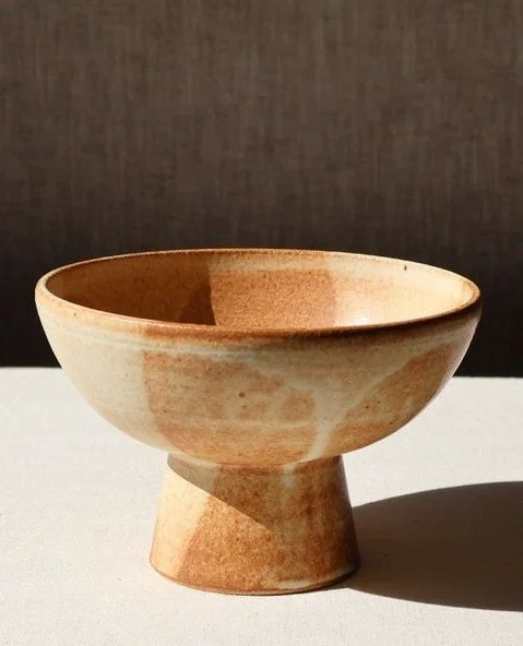 Another rusty dynamic glaze. This stoneware pedestal bowl sits low and wide, balanced on a narrow foot. The surface catches a brown-to-cream, matte. Fired in reduction it has lots of glaze variance and detail. Solid but open, it&rsquo;s a piece made 