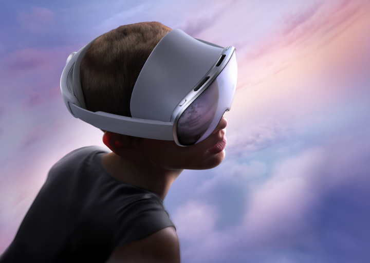 A young boy wearing a virtual reality headset, looking upwards at a colorful sky with clouds during sunset.