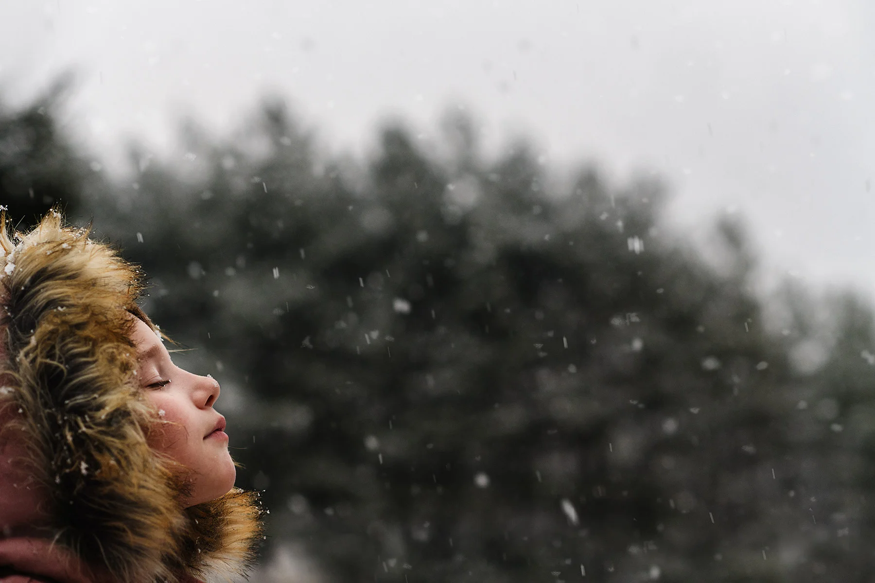 girl with face up toward snow in fur hooded coat kellie bieser.jpg