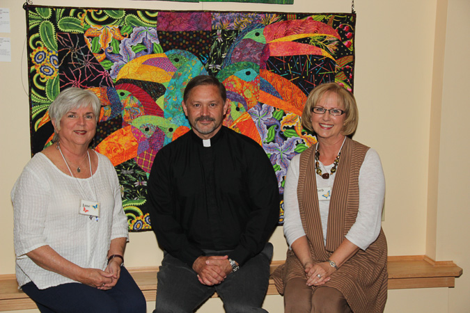 Jane Oliver and Barb Redmond, co-charis of the exhibition, with Fr. Bill Breedlove in front of Toucans by Lucinda Graber of Upland, CA.