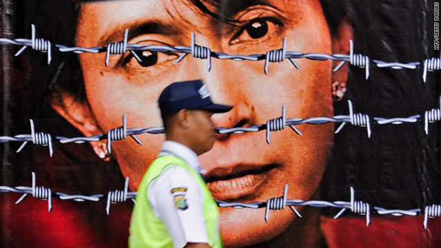 A guard walks past a huge poster of Aung San Suu Kyi (source: CNN)