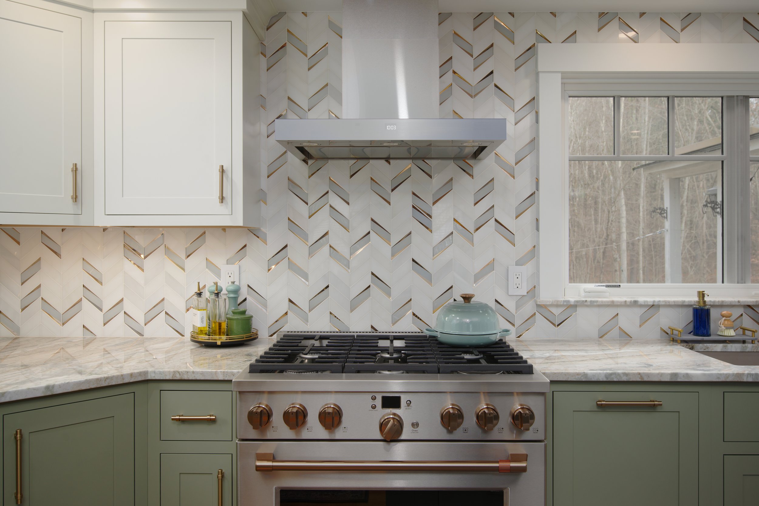 Custom kitchen with sage green and white cabinetry, a stainless steel range and hood, marble-look countertops, and a geometric tile backsplash