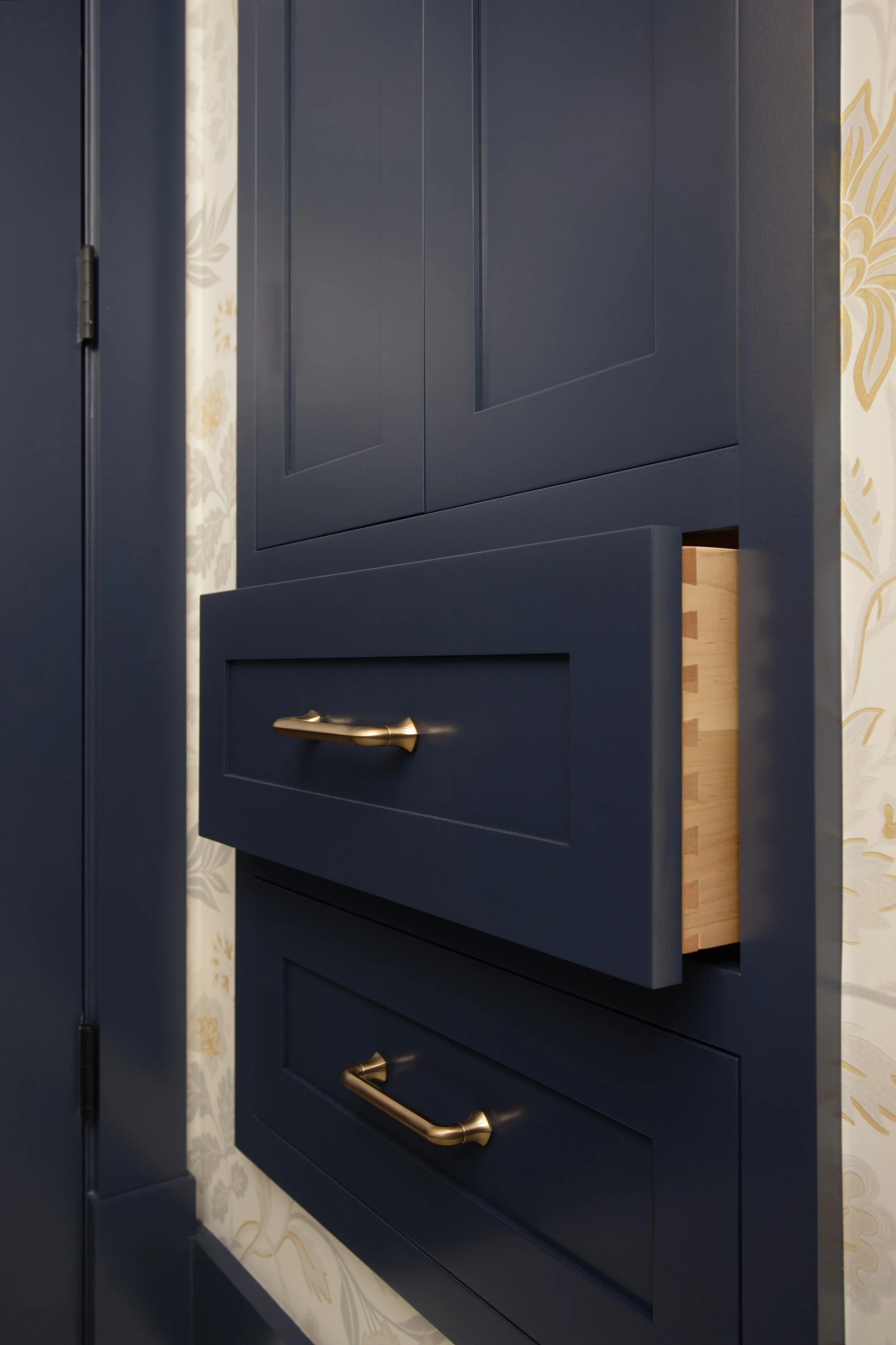 Custom navy built-in bathroom cabinetry with inset drawers, dovetail construction, brass hardware, and floral wallpaper