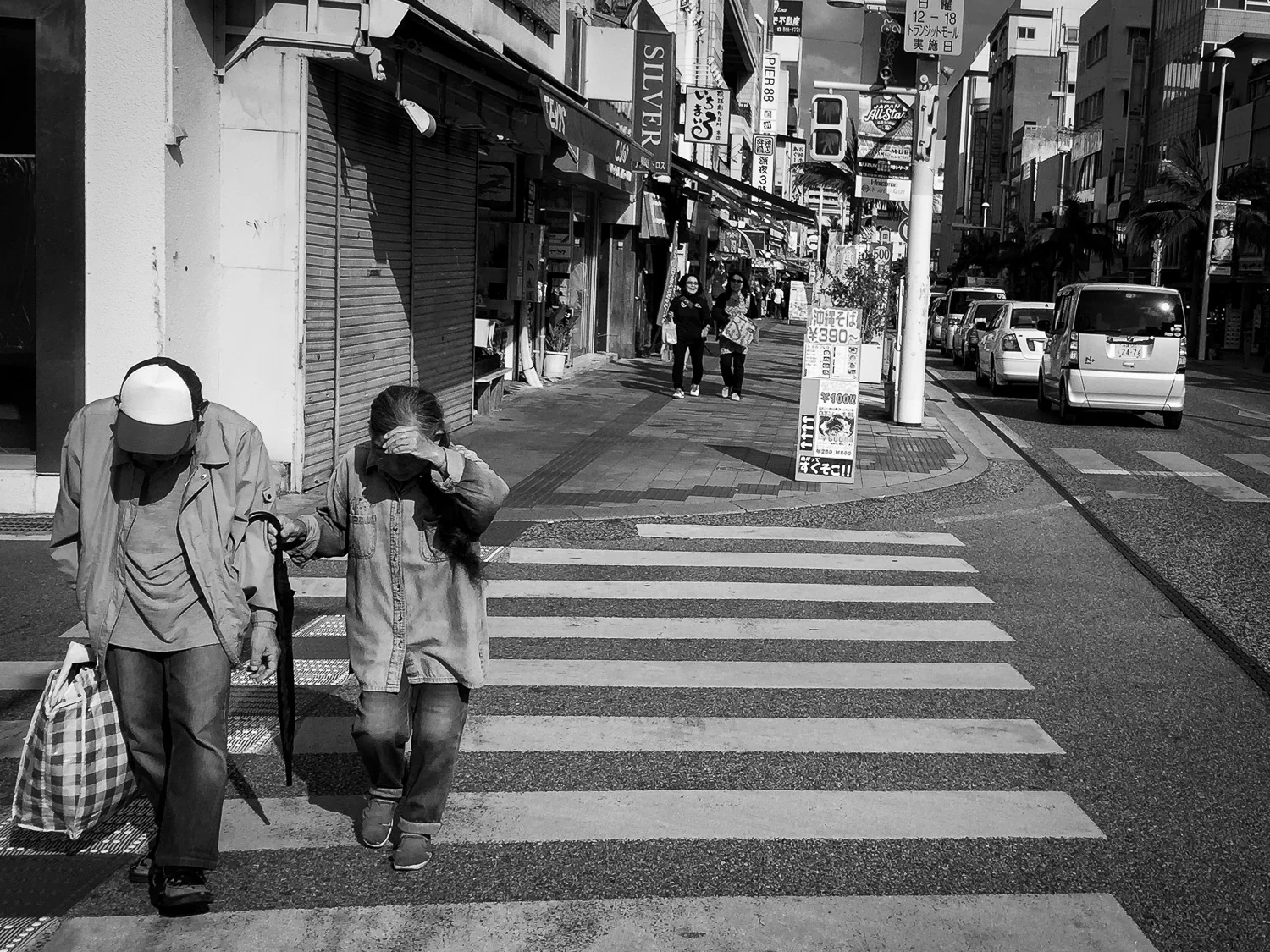 An elderly couple crossing the street in Naha, Okinawa, Japan. Apple iPhone 6 Plus at ISO 32, f2.2, 1/4000 sec. Converted to black and white in Lightroom Mobile.
