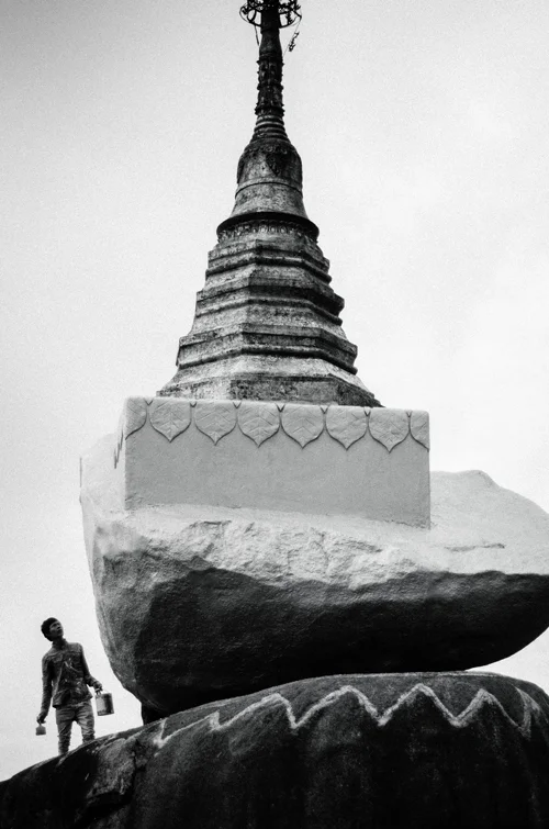 A man painting a smaller balancing boulder, near the entrance to the complex.