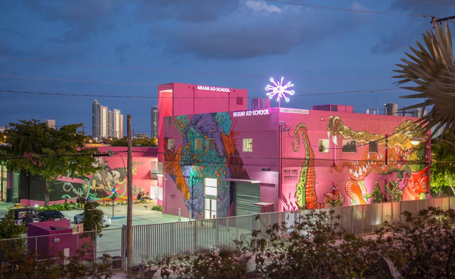  With the city skyline in the distance, this new academic campus and headquarters utilizes its entire site. The existing and new structures were given visual cohesion with a coat of bright pink paint, the school’s signature color. 