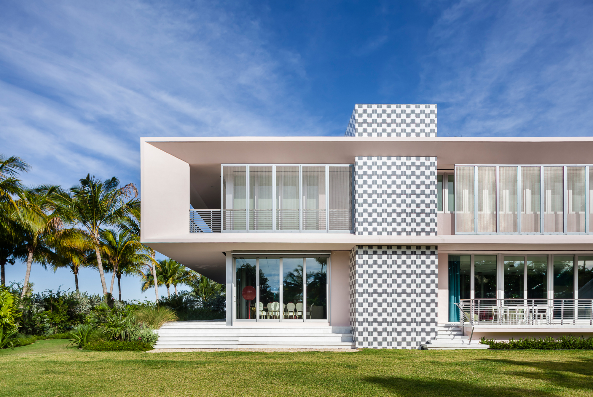  Tweaking a horizontal typology   The house features a formalist frame - painted in a light blush pink - that catches the differing qualities of light in Miami. A tiled column adds a Memphis touch to the exterior. Overhanging canopies shade ribbon wi