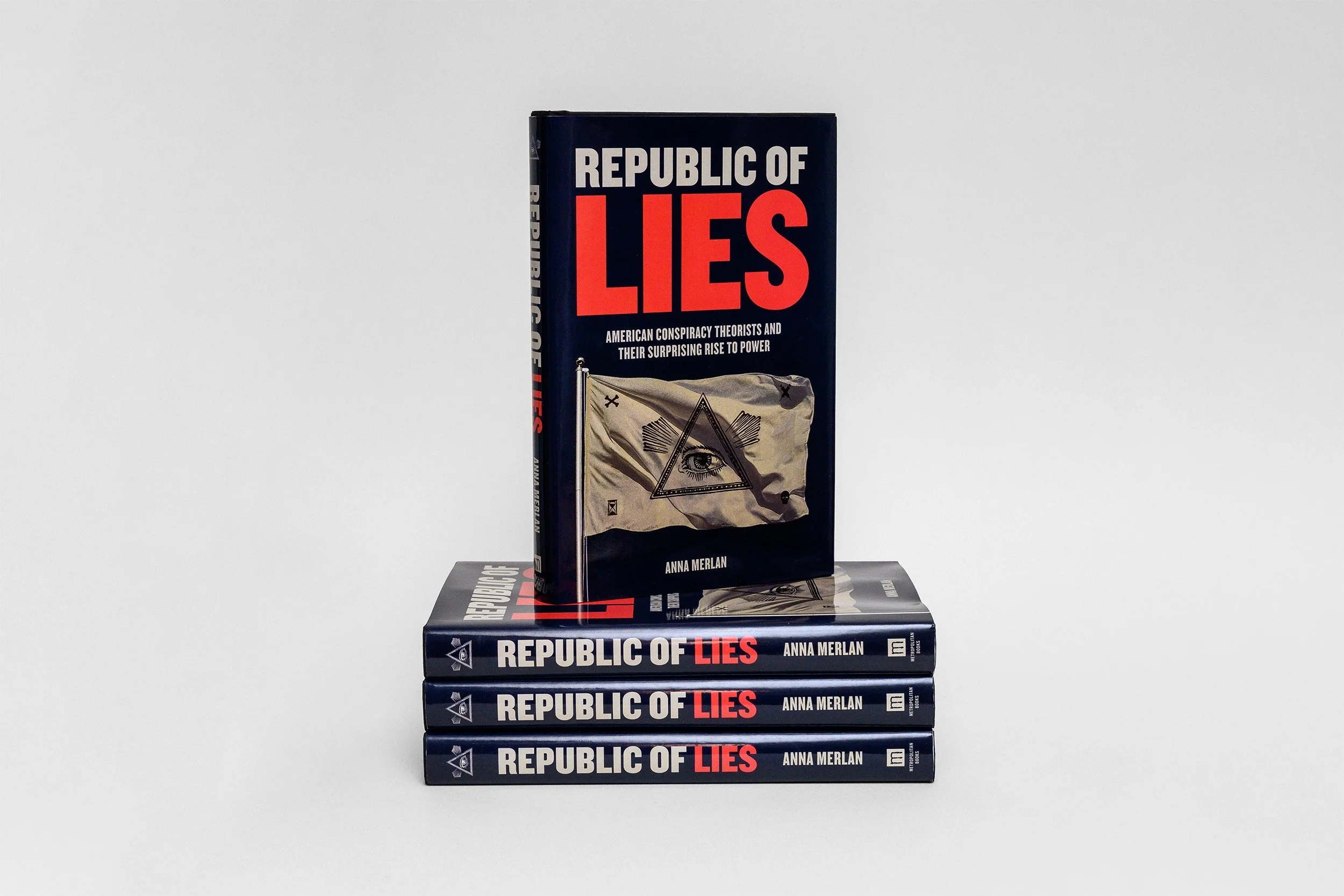 Four copies of the book titled "Republic of Lies" by Anna Merlan, one standing upright on top of three stacked lying flat, against a plain white background.