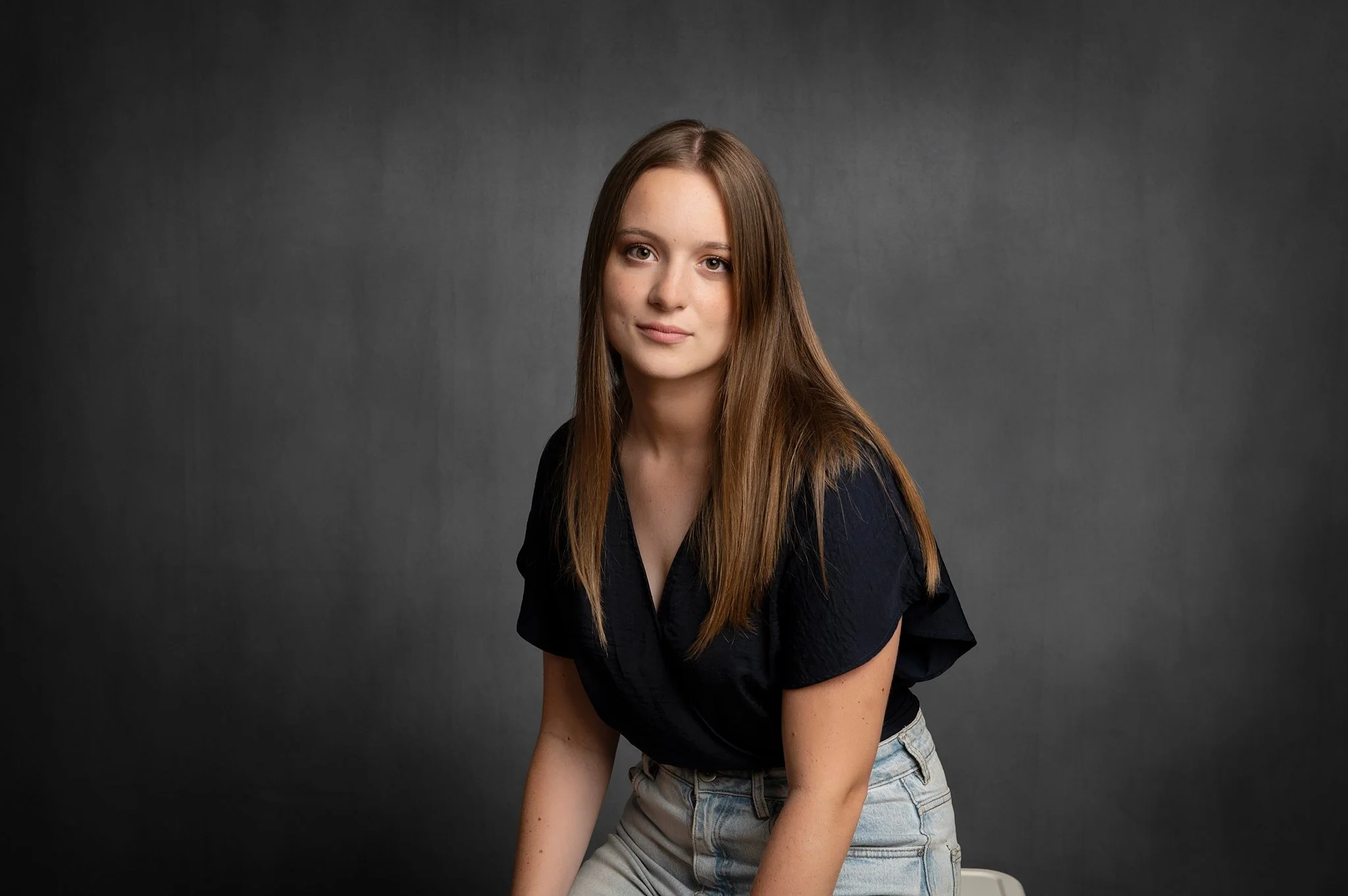 Woman with a composed, professional expression in an executive headshot on a dark studio background