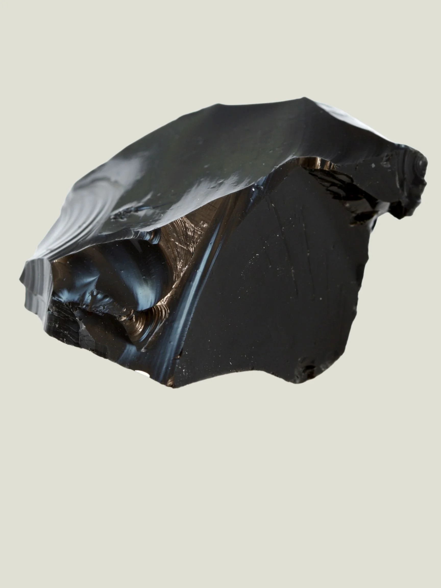 Close-up of a black, rough-cut piece of obsidian mineral against a plain light background.