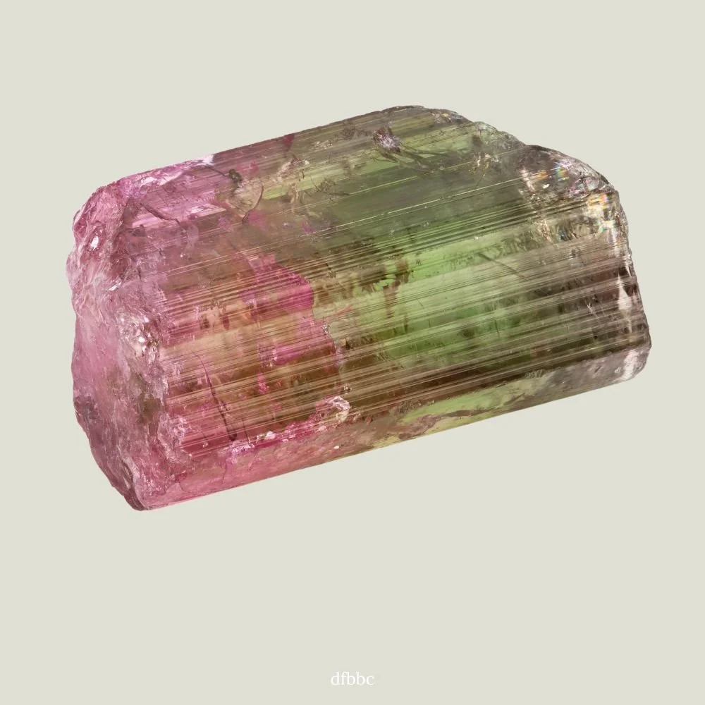 A large, partially transparent crystal with pink and green hues, showing striations and internal reflections.
