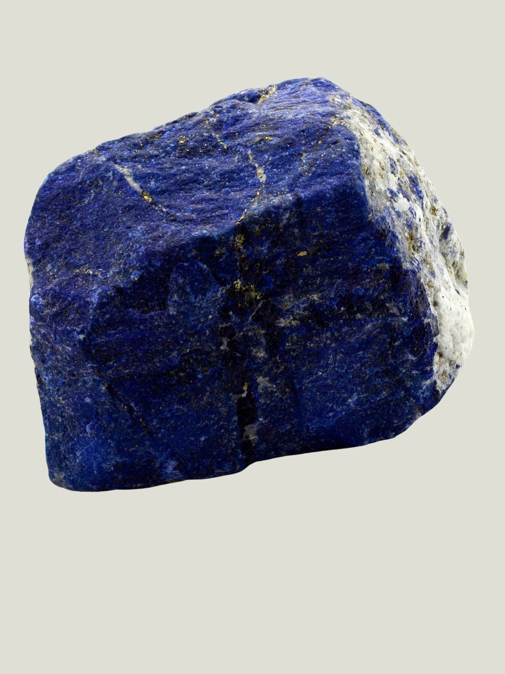 A rough, unpolished blue mineral or gemstone, possibly lapis lazuli, with some white and gold streaks, on a plain white background.