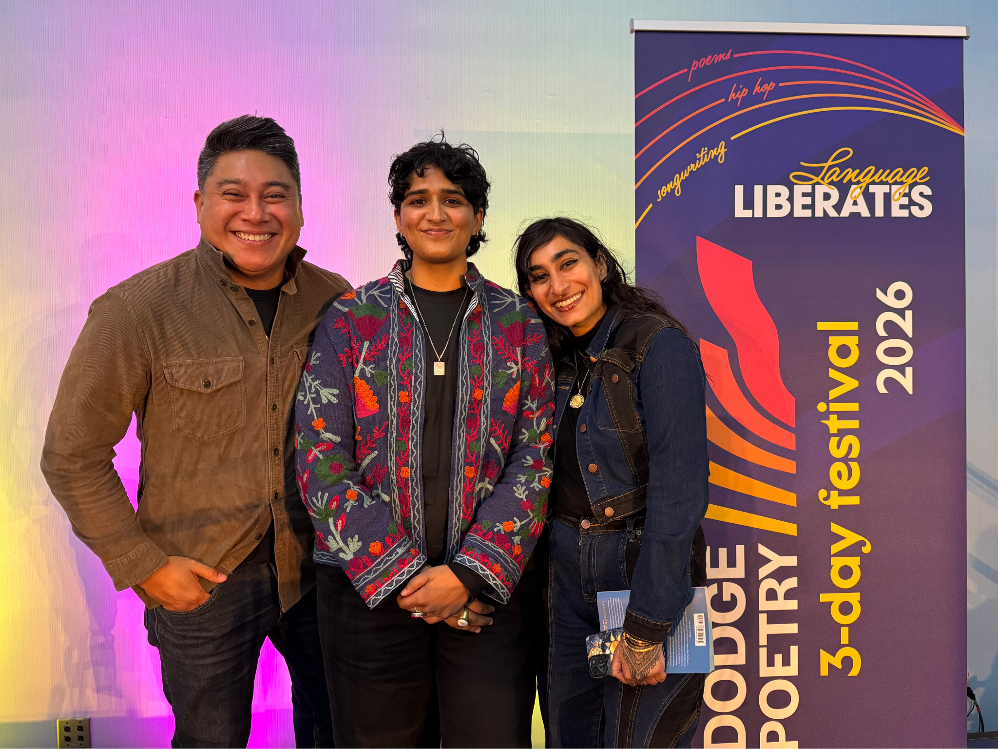 Three writers pose beside the poetry festival banner.