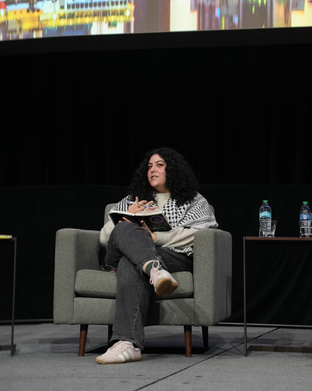 leena aboutaleb sits on an armchair on stage, moderating the discussion.