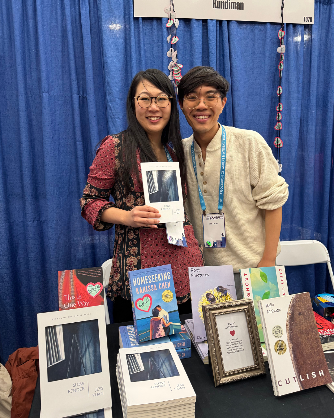 Jess Yuan holding up her book and standing beside Wo Chan at the Kundiman booth