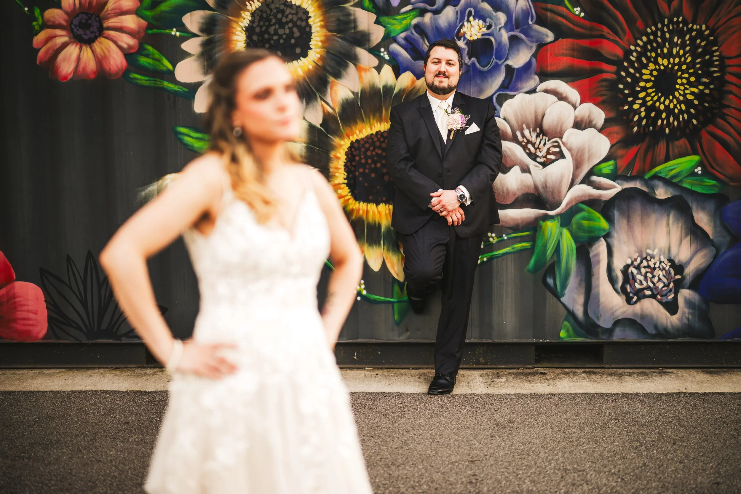 The groom admires his bride while leaning against a rustic "flower wall" at The Design Barn in Hebron, Indiana.