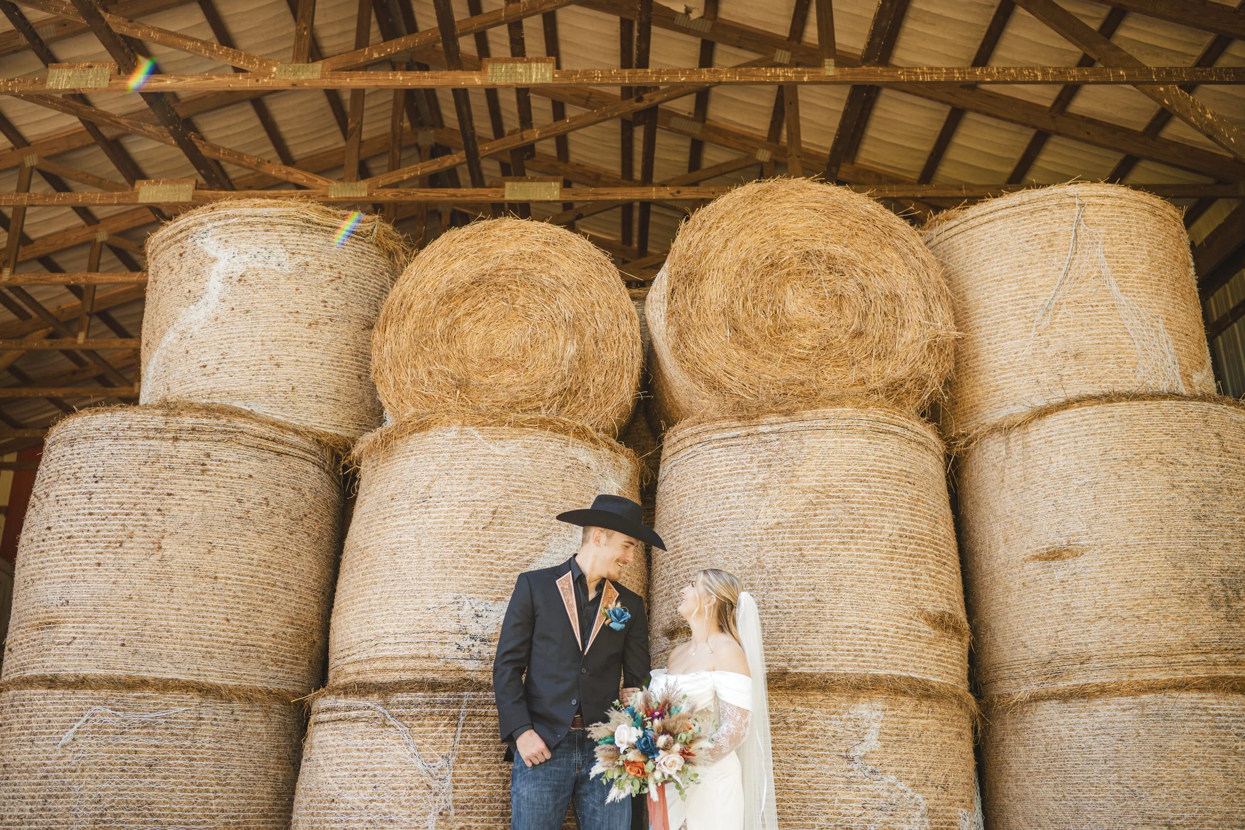 A bride and groom stand in front of stacked hay bales on a private Indiana farm.