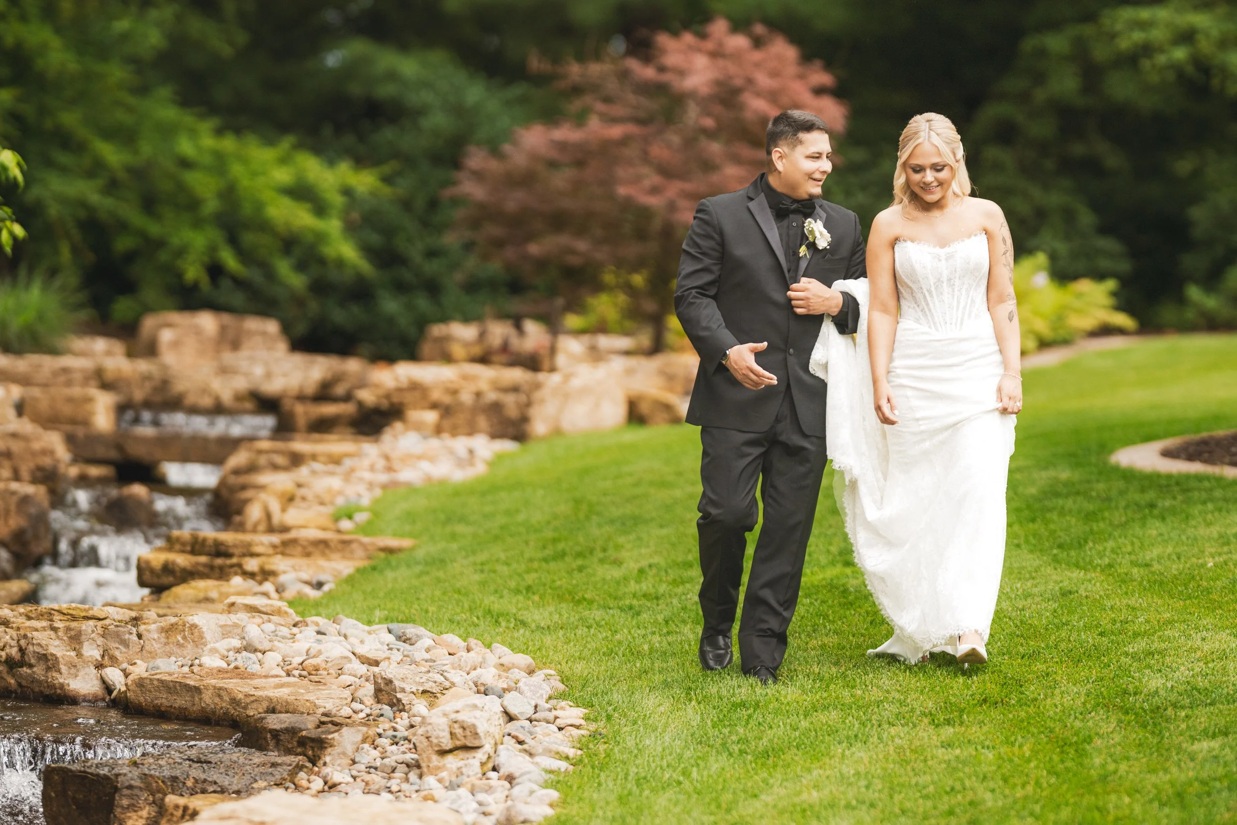 Bride and groom take a stroll along a stream at Sandy Pines golf course.