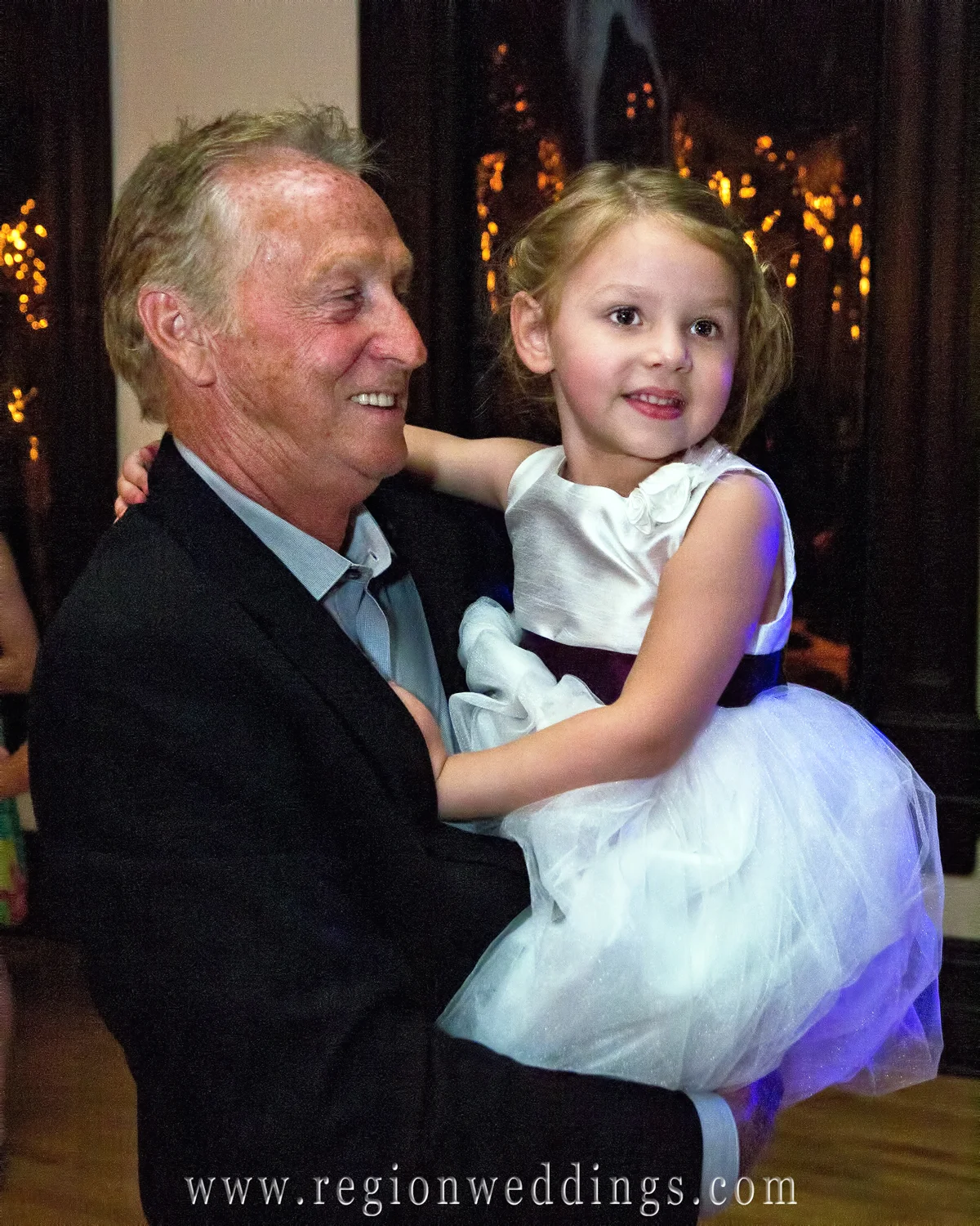 A grandfather dances with the flower girl in this fun, candid wedding photo.