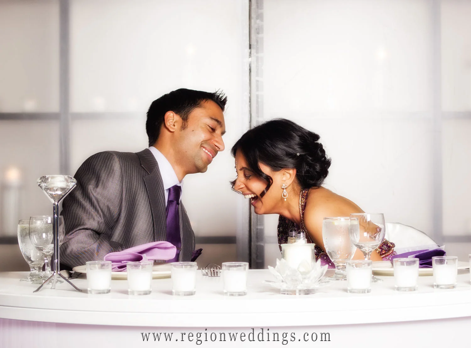 Candid wedding photo of bride and groom laughing at the head table of their wedding reception at the Radisson Hotel in Merrillville.