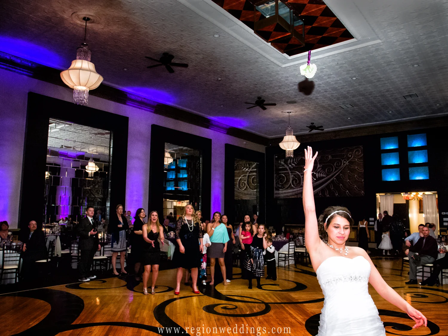 A bride tosses her bouquet at The Allure ballroom in Laporte, Indiana as beautiful purple uplighting fills the room.