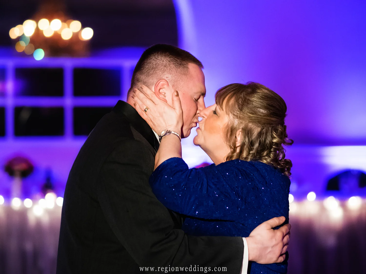 Mom give her son the groom a kiss on the dance floor at his wedding reception.