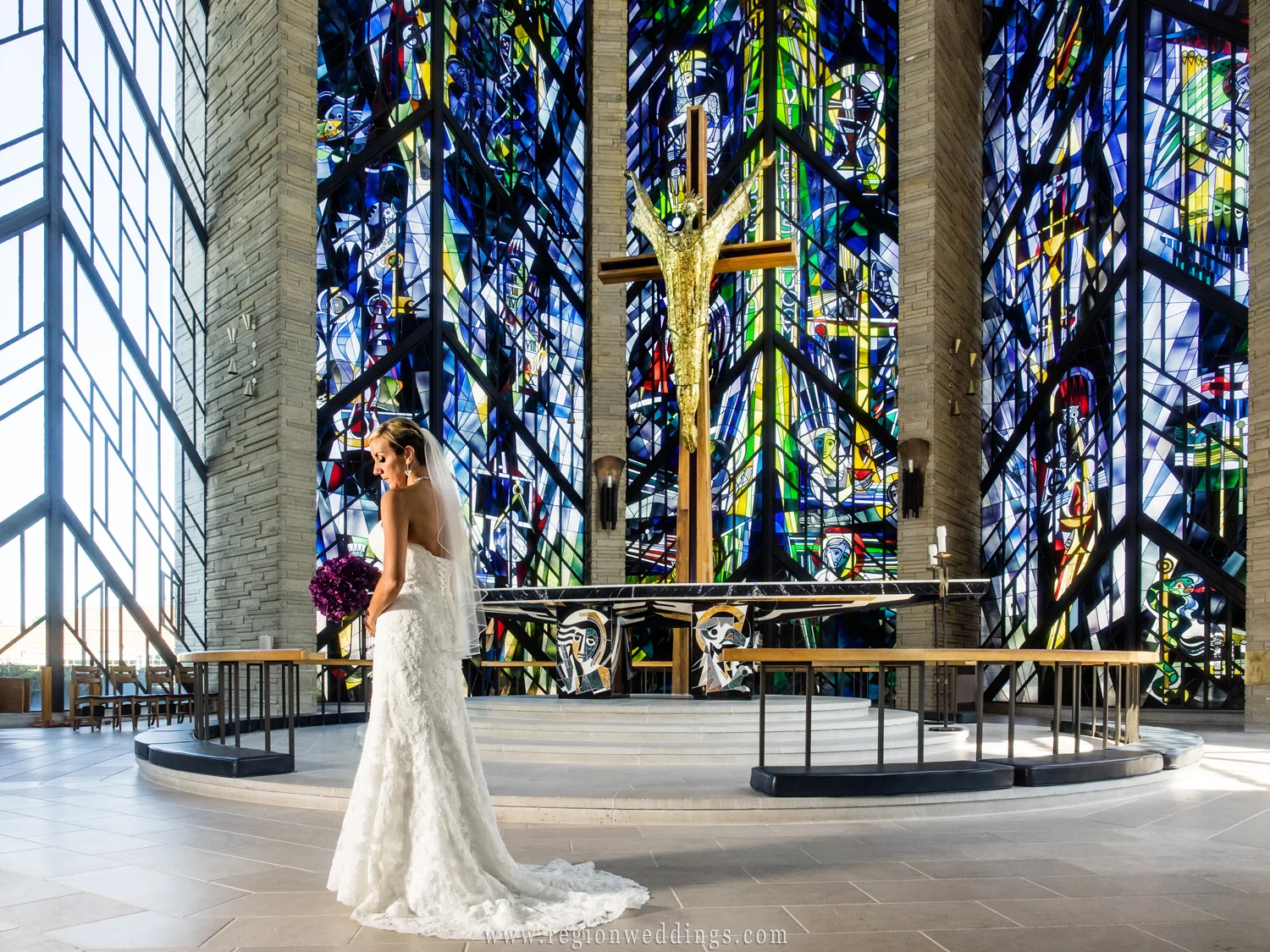 The bride alone at the altar in front of stained glass windows.