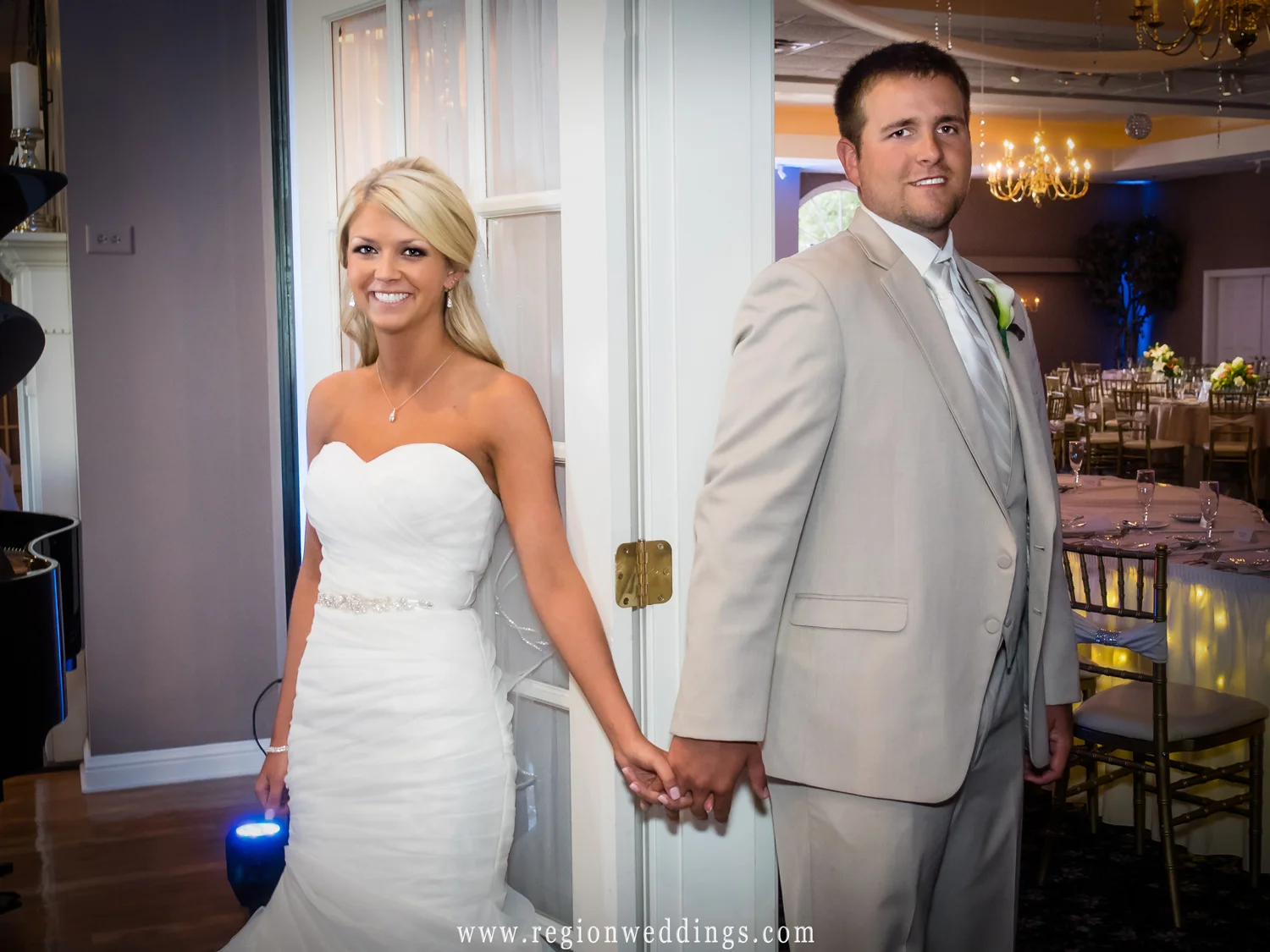 The bride and groom hold hands as they stand at opposite sides of a doorway.