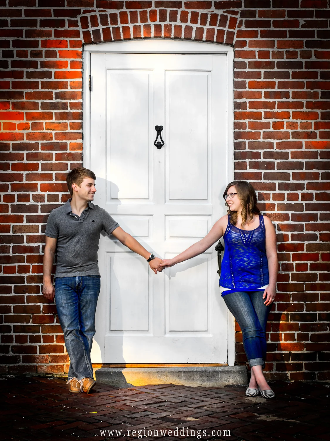 An engaged couple holds hands in between a doorway surrounded by brick at Deep River Park.