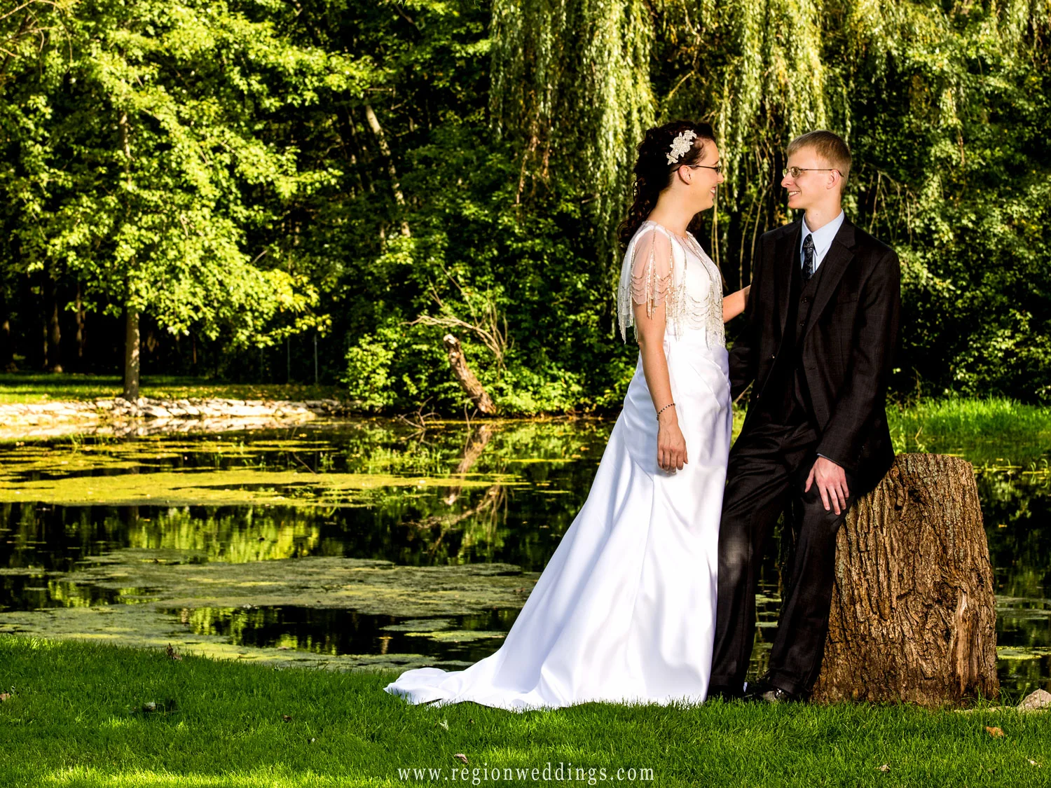 Beautiful greenery reflects into a small pond as the bride and groom gaze at each other.