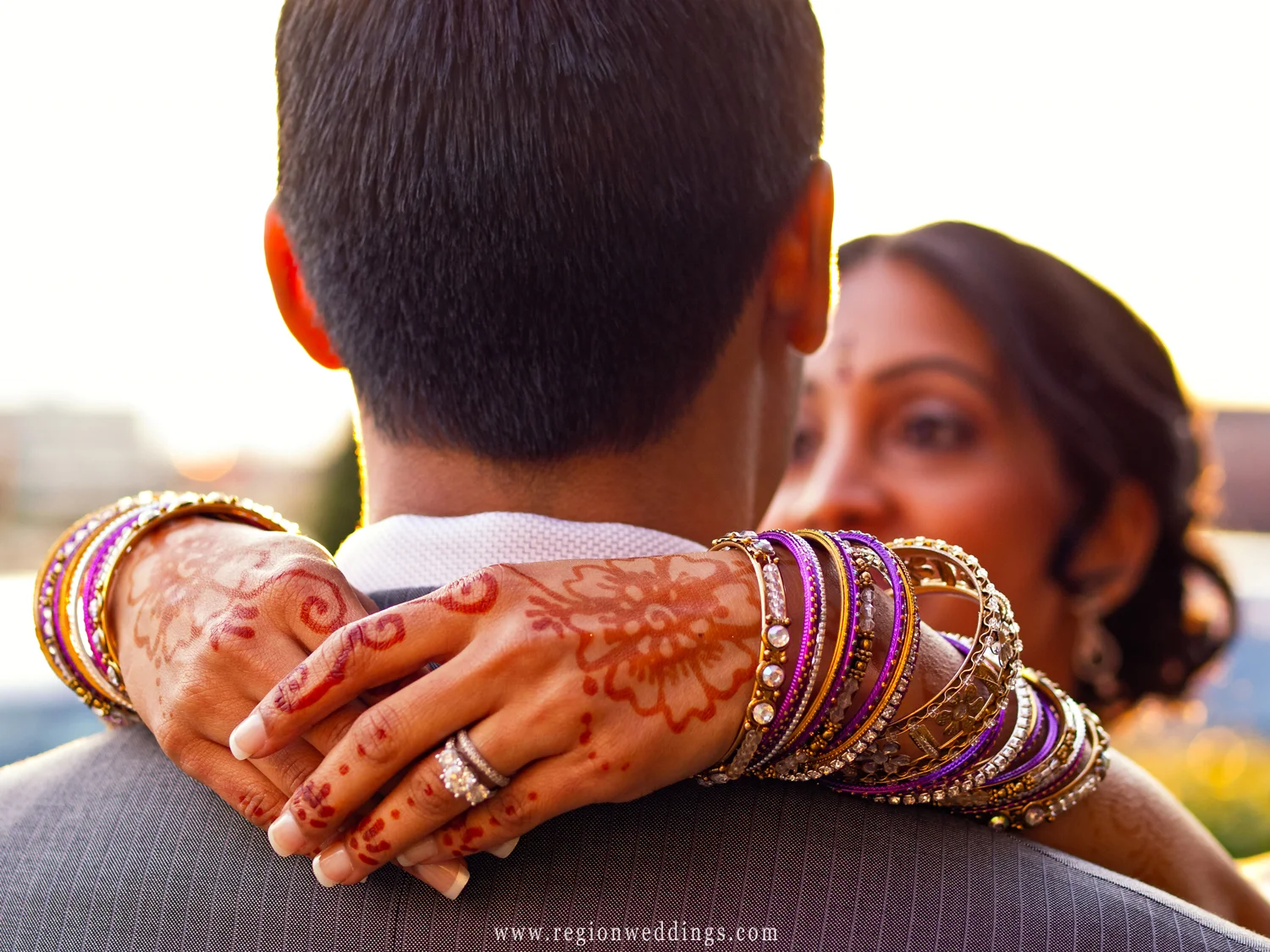 An Indian bride shows off her henna decorated hands as she embraces the groom.