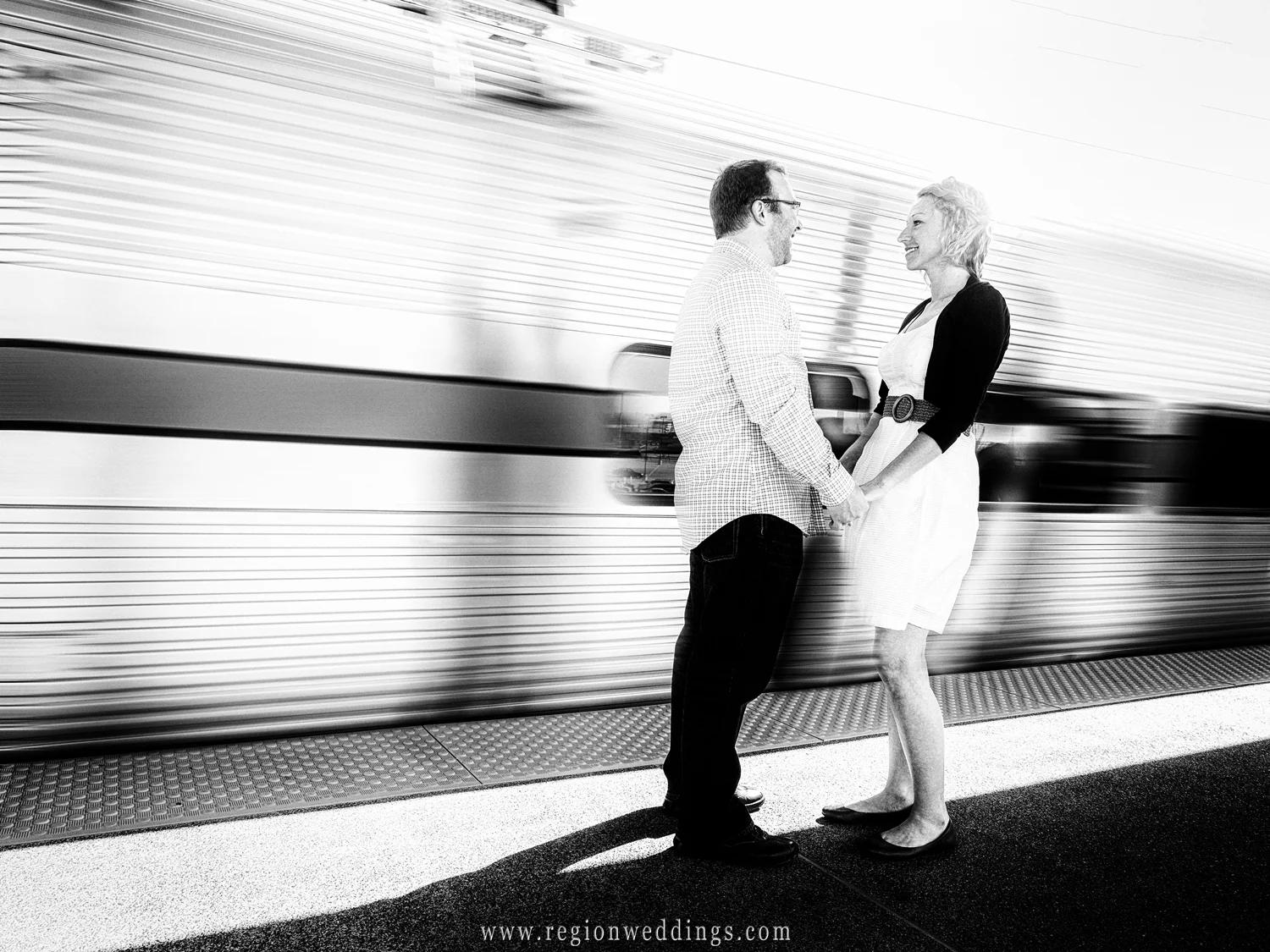 The train speeds by a couple on the train platform for their engagement photo.