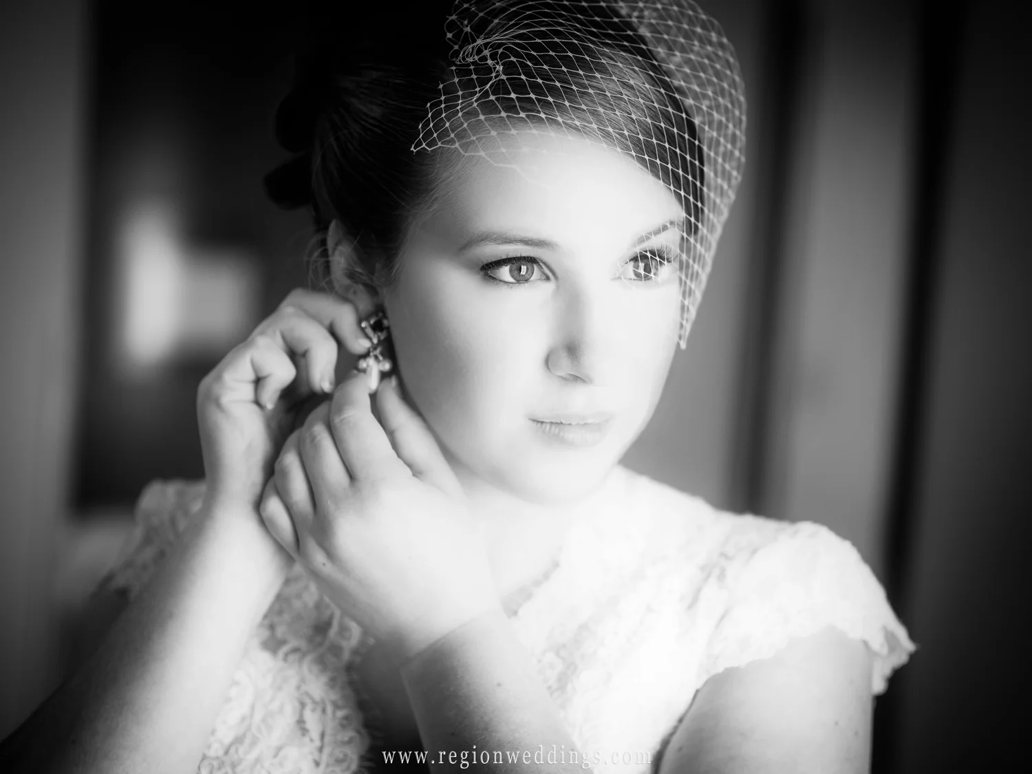 The bride puts on earrings as window light shines upon her.