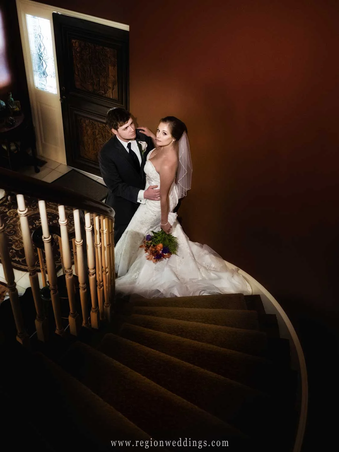 The bride and groom embrace at the bottom of a staircase.