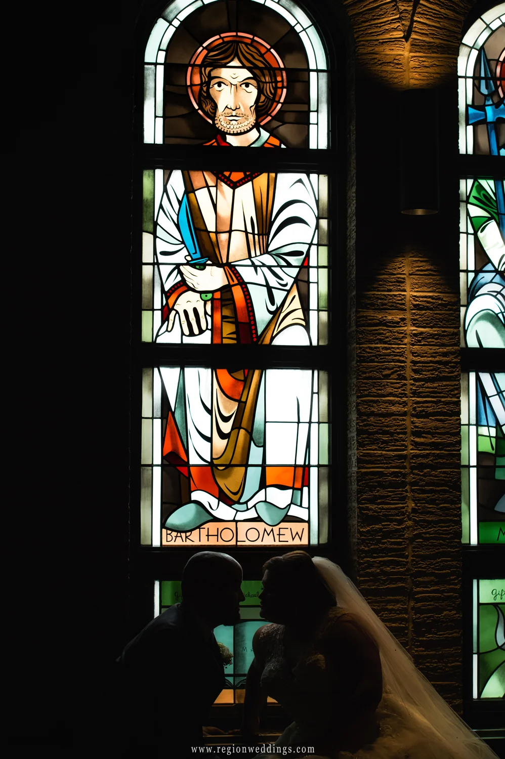A silhouette of the bride and groom in front of stained glass windows at Saint Maria Goretti Church in Dyer, Indiana.