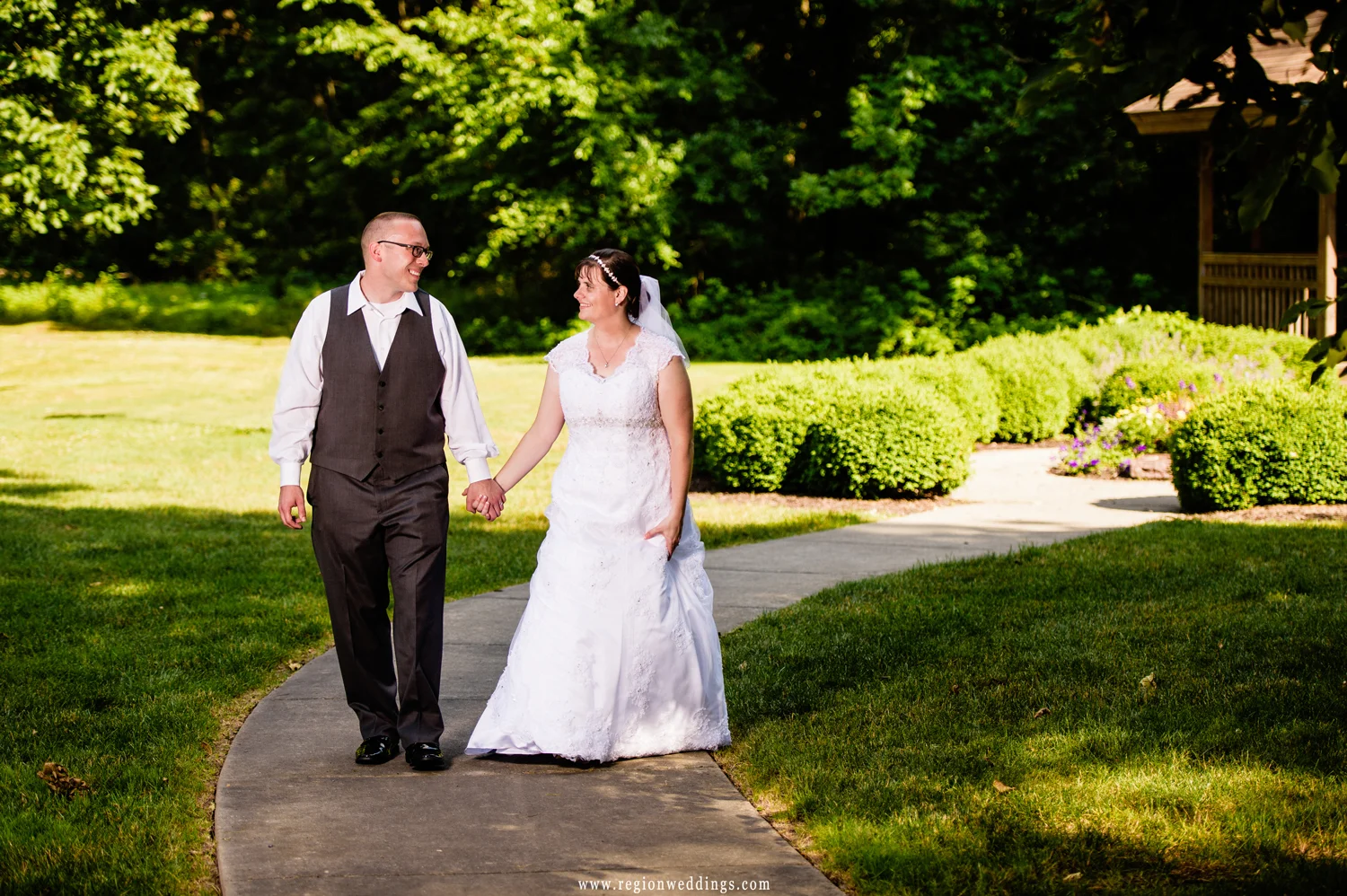 The bride and groom take a stroll in a Crown Point park with a gazebo in the background.