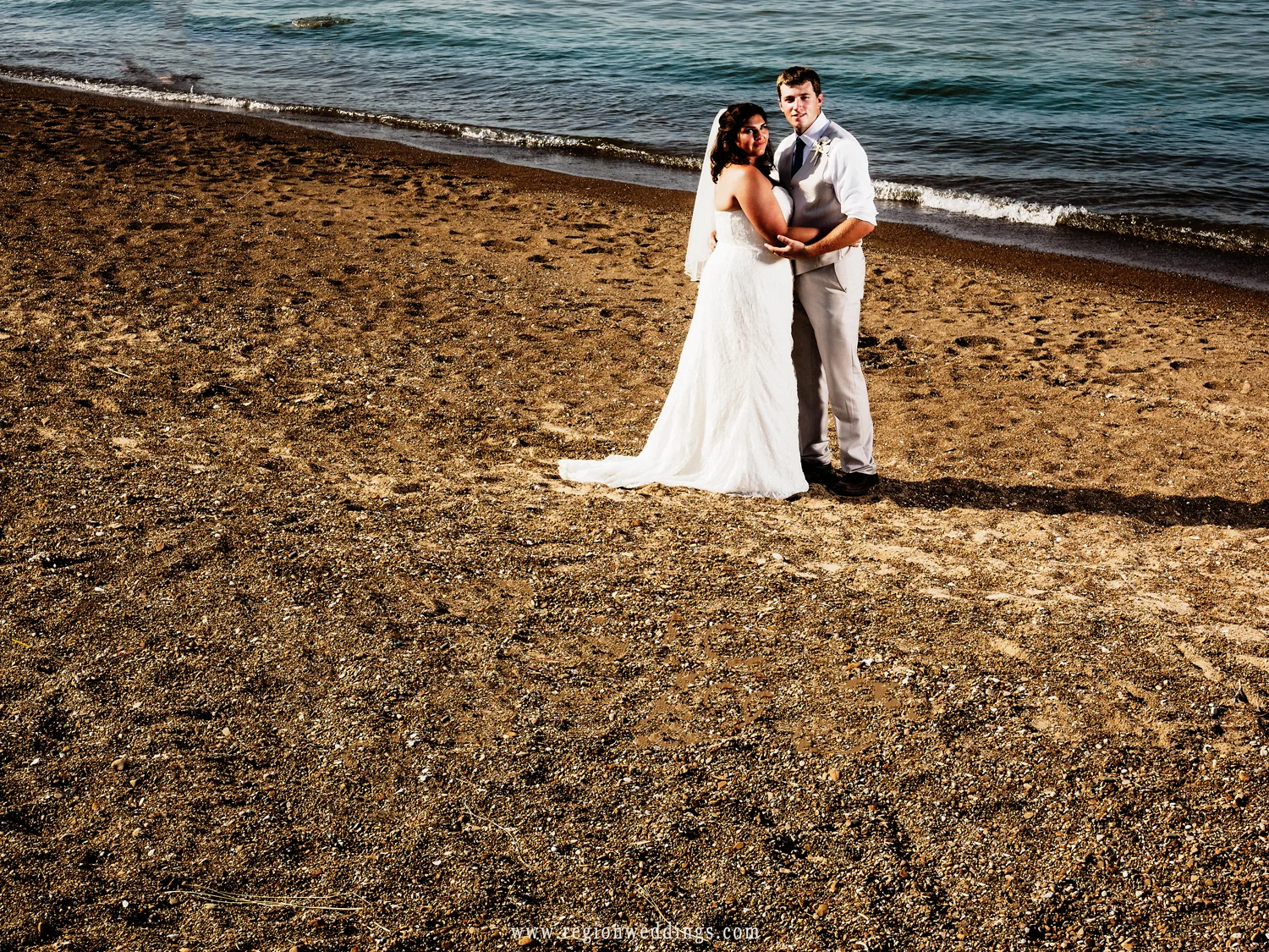 The bride and groom on a Lake Michigan beach as waves roll onto the shore.