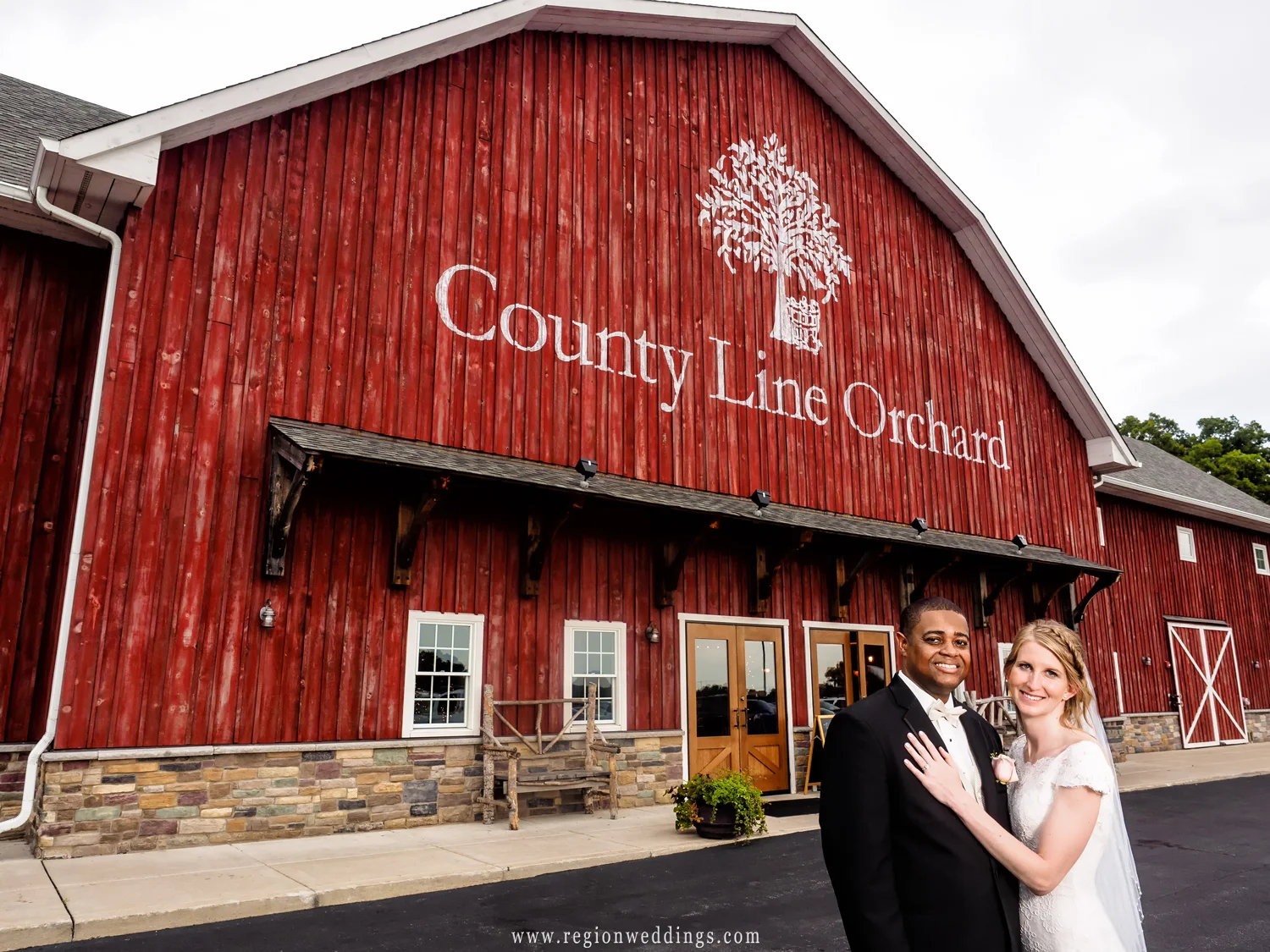 The bride and groom in front of the big red barn of County Line Orchard.