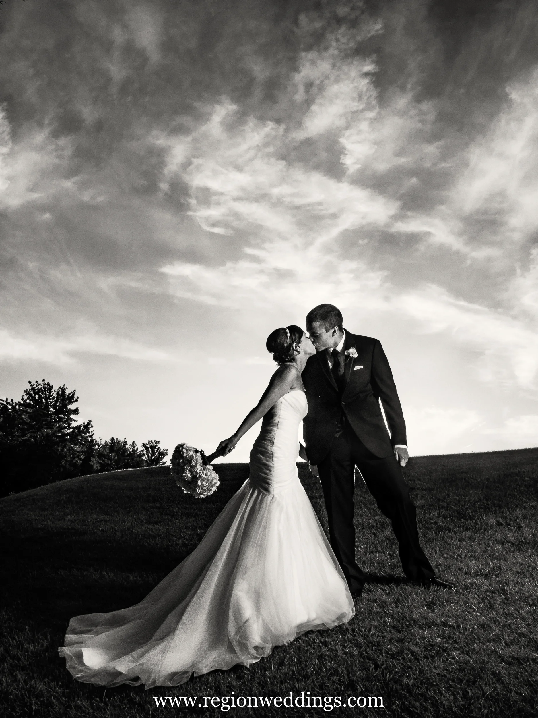 Black and white photo of bride and groom kissing on a hill at White Hawk Country Club.