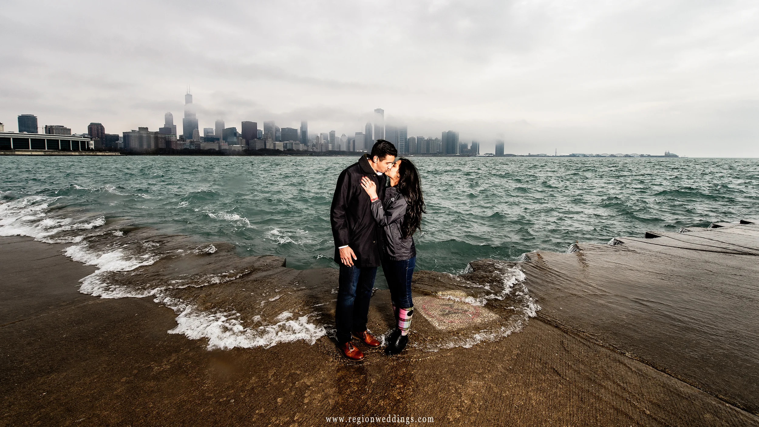 Waves from Lake Michigan crash onto the boardwalk during a Chicago engagement session.