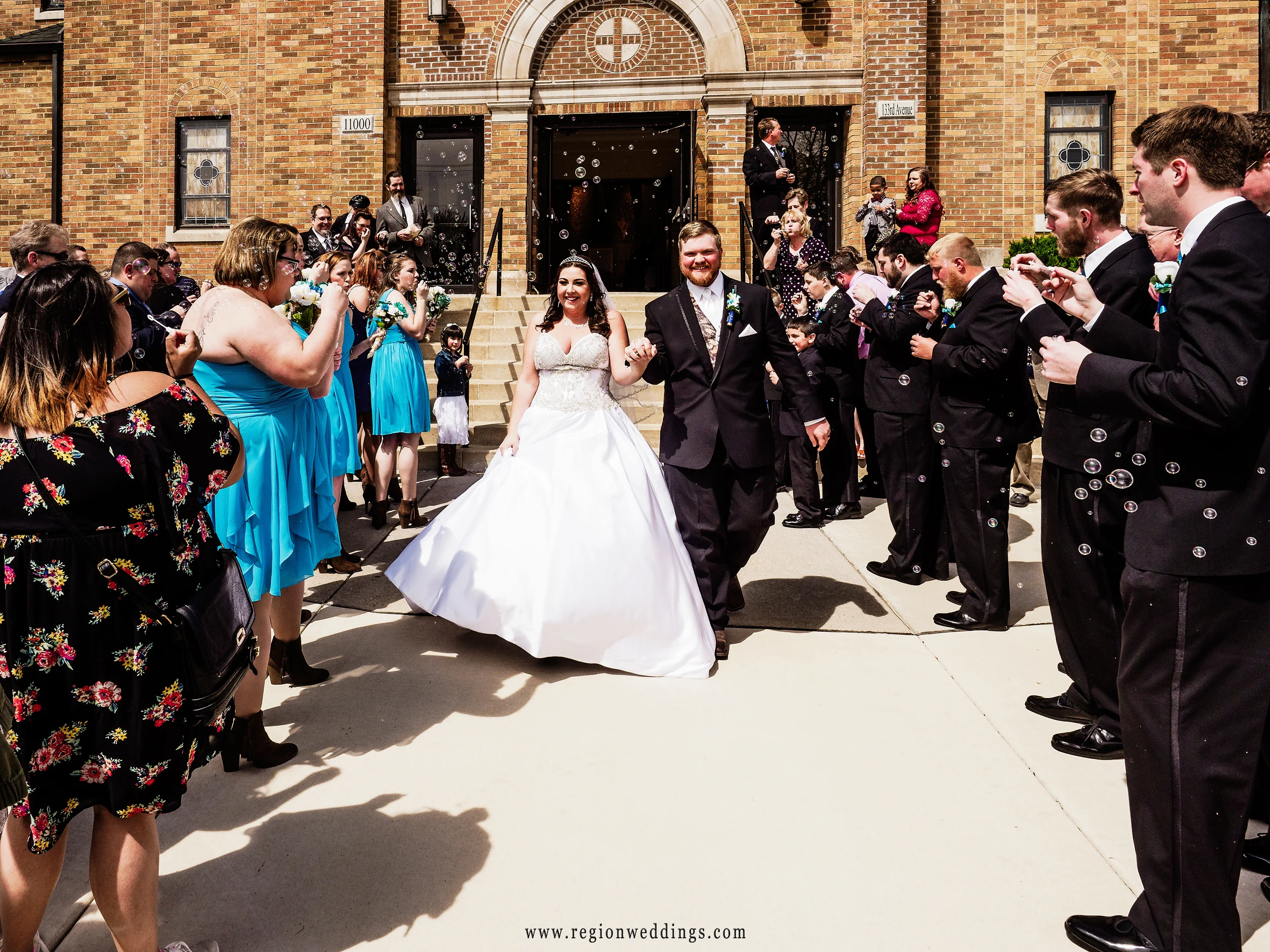 The bride and groom walk through bubbles as they exit church at their Spring wedding.