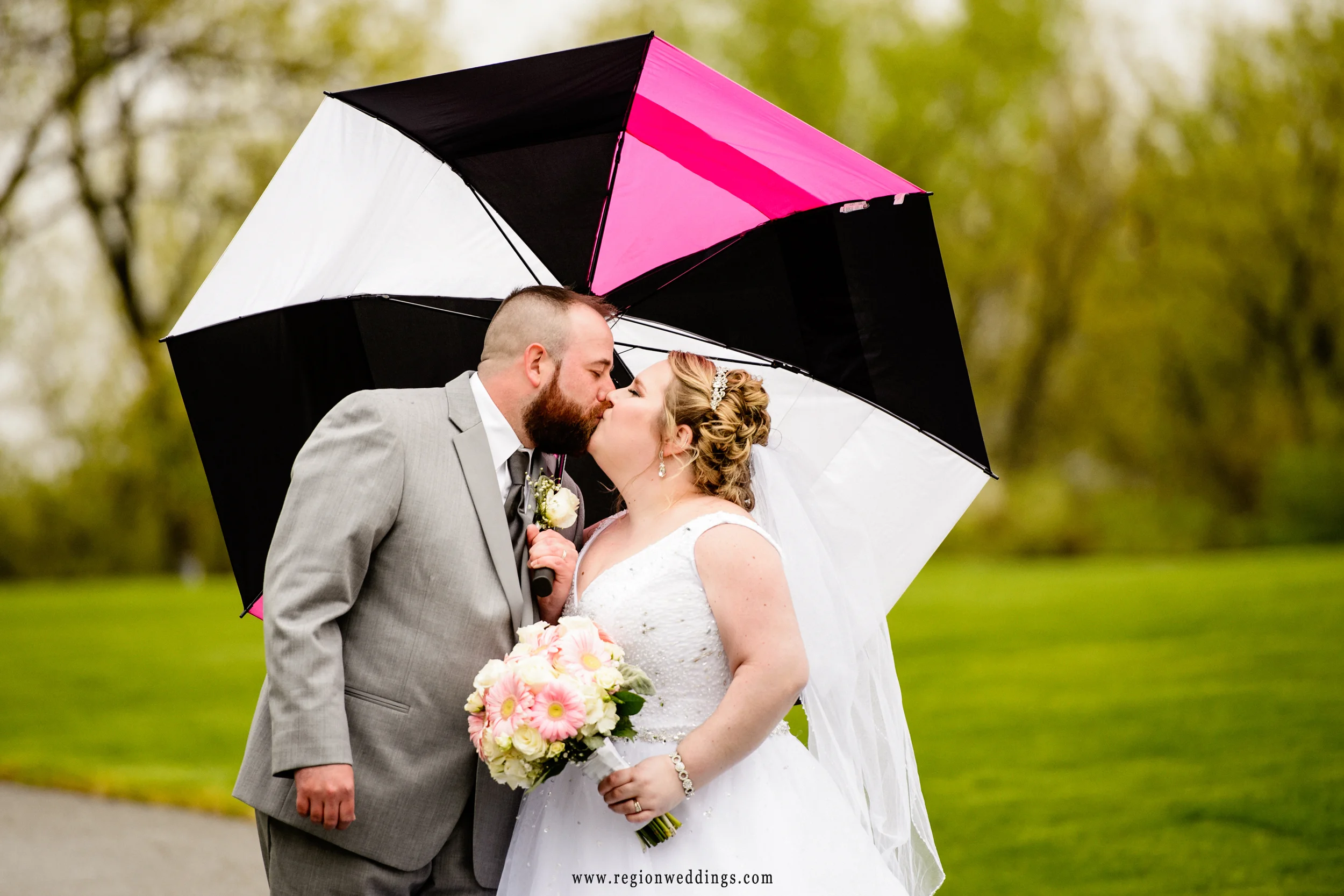 Bride and groom underneath a pink and black umbrella.