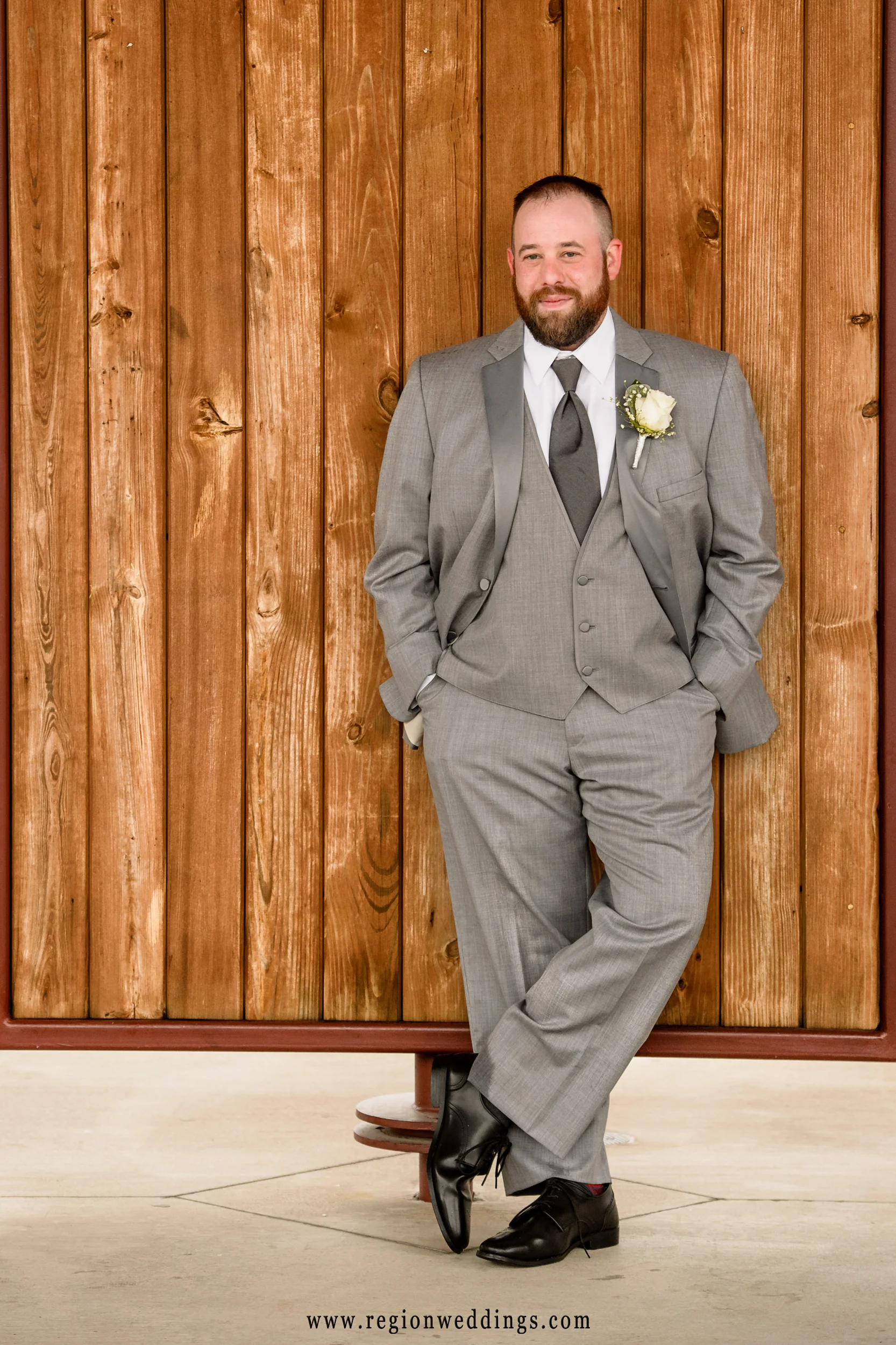 The groom leans against the wall of the amphitheater at Centennial Park.
